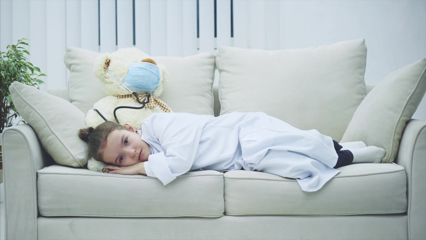 Little girl in medical coat is lying on the bear