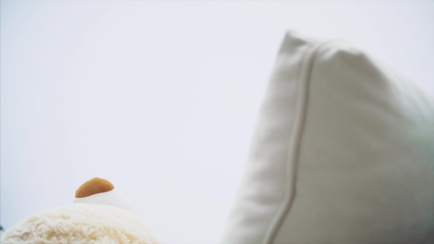 Small girl with plaits putting white teddy on the sofa, covering it with a blanket, going away.