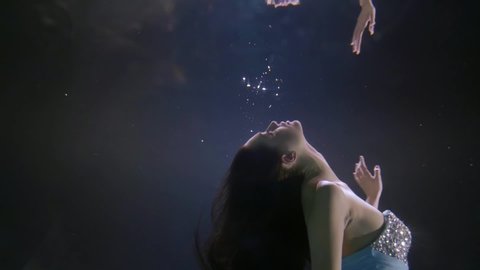 portrait of a face in profile of a dark-haired girl with rhinestones on her face who is underwater, the delicate fabric of her dress and her hair developing. It reflects off the surface of the water.