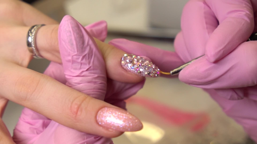 Macro shot with manicurist that sticks rhinestones to the painted nails, makeup and nails, close up of applying nail polish. Royalty-Free Stock Footage #1043289940