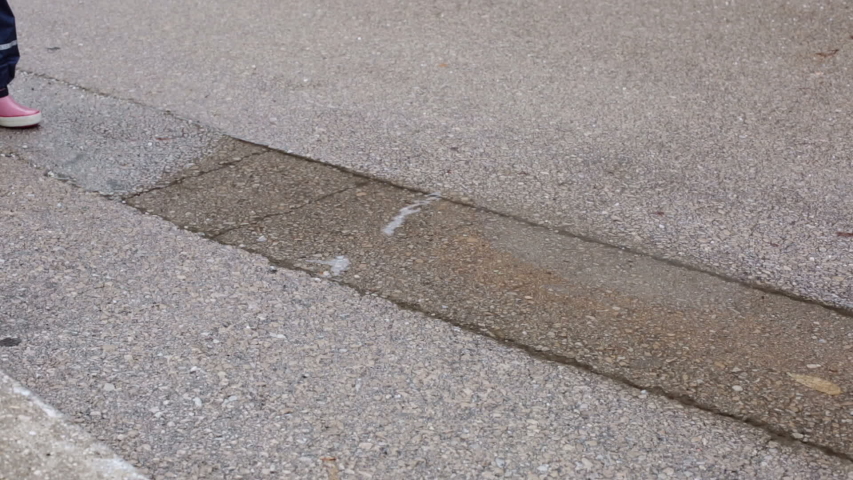 Girl child jumping in puddle splashing water in autumn rainy day