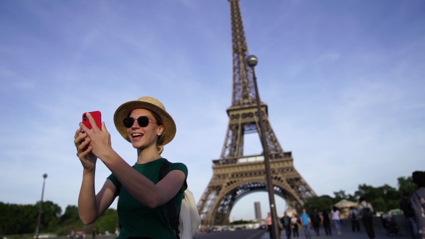 Slow motion of happy young woman tourist walking in France and talking with friend via video call on smartphone using roaming.Positive traveler waving hand at front camera standing near Eiffel Tower 
 | Shutterstock HD Video #1043303425