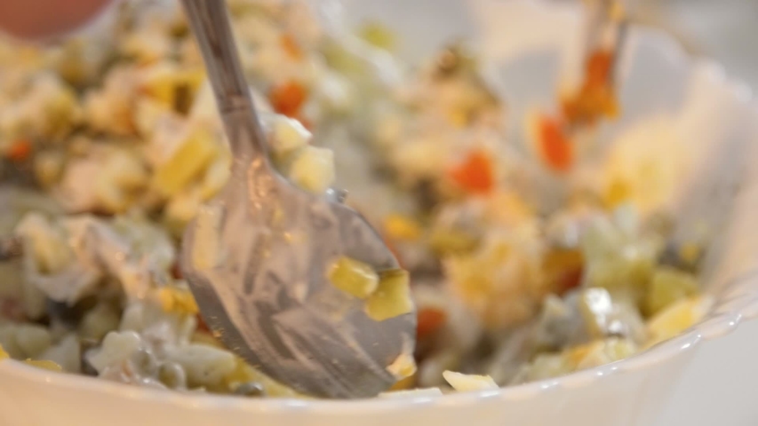 Mixing colorful salad with boiled vegetables in white bowl closeup