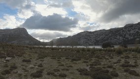 4K panoramic footage of beautiful mountain landscape with highland lake. Dramatic cloudy sky. Sheeps graze in the grassland. Winter on Mallorca island, Sierra de Tramontana 