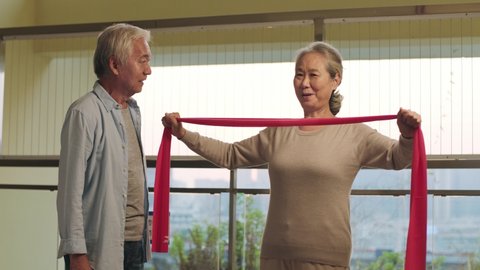 happy senior asian couple exercising with resistance band
