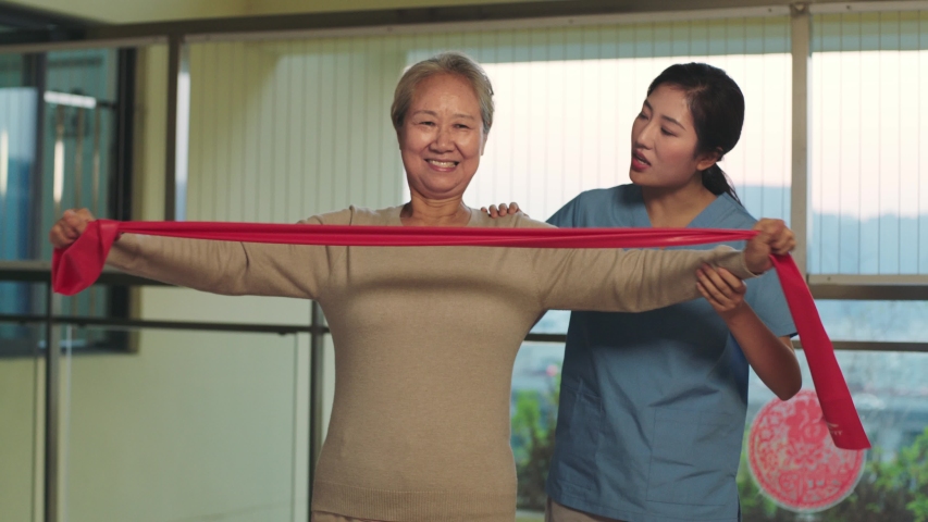 senior asian woman rehabilitating using resistance band with help from female physical therapist Royalty-Free Stock Footage #1043314198