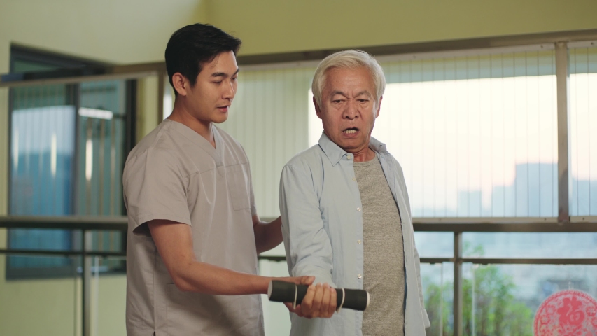senior asian man rehabilitating using dumbbell with help from physical therapist Royalty-Free Stock Footage #1043314333
