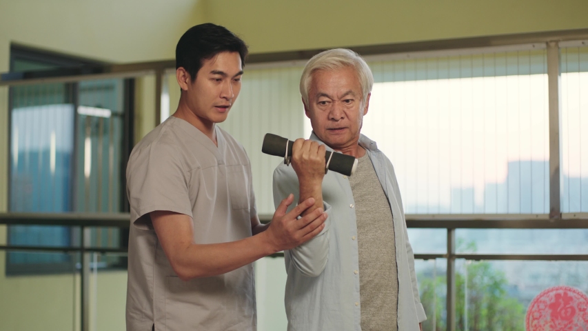 Senior asian man rehabilitating using dumbbell with help from physical therapist | Shutterstock HD Video #1043314333