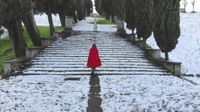 Woman with red coat climbs an ancient staircase, outdoors, on a winter day with snow