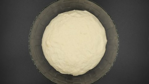 Yeast dough rising in glass bowl on black background, top view.