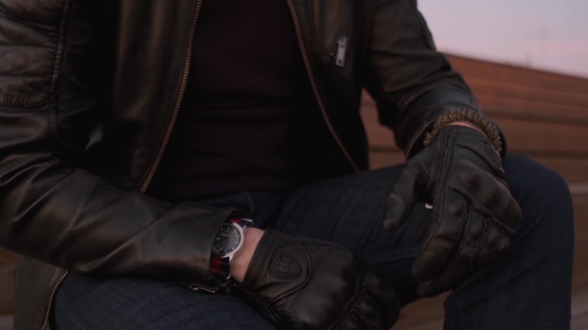 Close-up, a Man in a leather jacket and gloves looking at his watch.
