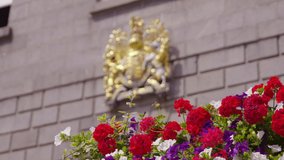 A daylight long shot of a crest in gold finish affixed on the exterior wall facade of a building near a colorful blooming flowery plant. - Powered by Shutterstock - Get 15% off with code: PIKWIZARD15