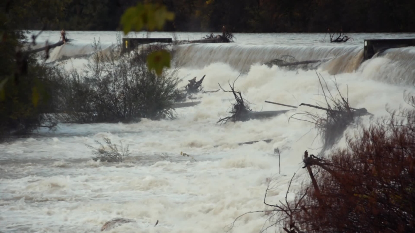 Static view of dirty river flooding over small dam with driftwood