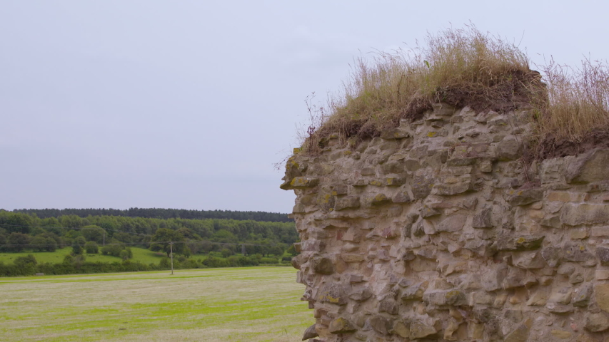 A still medium shot of a rockwall with trees on a hill in the background