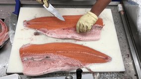 Japanese professional chef in gloves cutting, slices fresh of raw red salmon fish. Hands with a knife close-up. Fish factory, shop, production, commercial kitchen. Mediterranean diet. Norwegian salmon