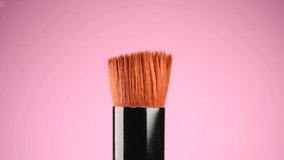 Make-up liquid foundation pouring on makeup brush, closeup. Foundation beauty facial cosmetics, Kabuki tool for perfect make up. Dripping bb cream or concealer, over pink background. 4K slow motion