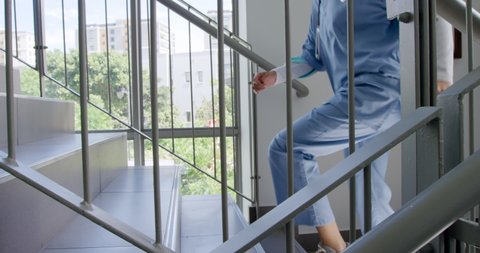 Low section side view of a female healthcare worker in uniform, wearing scrubs running up the stairs in a hospital. Healthcare workers in the Coronavirus Covid19 pandemic