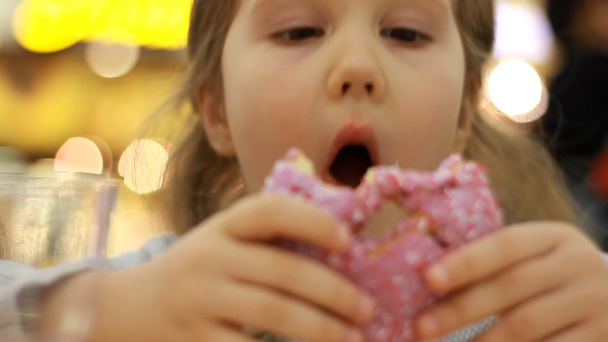 Child eats donut. Closeup baby girl eating doughnut with glase. Delicious, sweet, sweettooth.