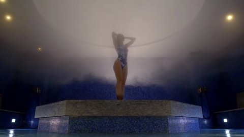sexy woman in swimsuit is inside hammam, standing alone and stroking her body