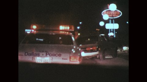1970s: Pan of police car driving. Tracking shot, driving toward police car stopped on road. Close up, man exits car. Man walks to cars on side of road.
