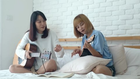 Asian teen girls learning guitars on bed at home on weekend, friendship and music lover