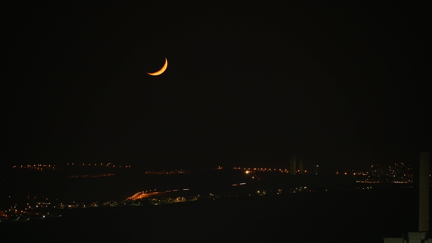 Cinematic 8K resolution 7680x4320 30p. Crescent moon disappearing at horizon line. Moonset at real true natural colors. Midnight night sky dark black down moonlight lune circle lunar city lights.