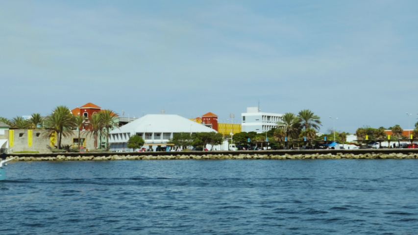 Beautiful view of coast line of Willemstad. Dark blue water surface of Atlantic ocean. Coast line with buildings merging with blue sky and white clouds. Willemstad. Curacao.