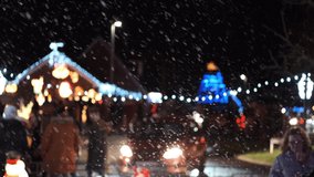 Winter night at the street with show falling from the sky and and blurred people and decorative Christmas lights on the background. Slow motion.