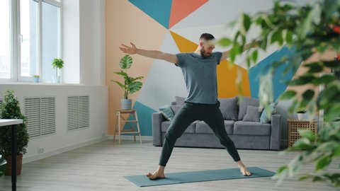 Professional yoga instructor in sports clothing is exercising at home doing complex of asanas alone standing on mat. Activity and apartment concept.