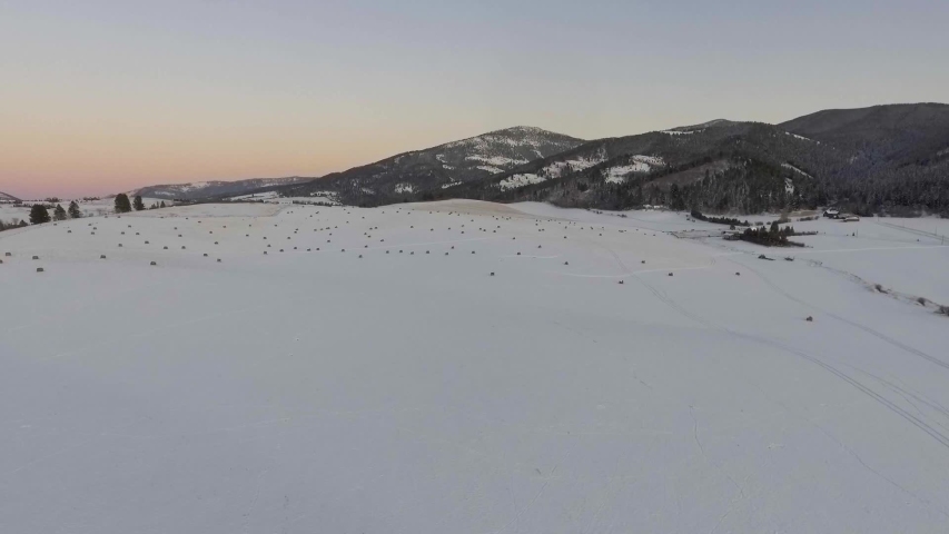 Drone flying high above snowy hay fields in cold Montana with beautiful mountains in the background