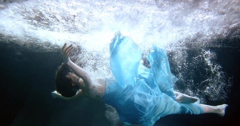 woman in blue dress is falling inside swimming pool, underwater shot