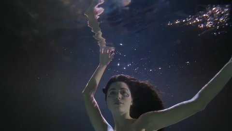 underwater view on swimming woman, stretching hand to surface with her reflection