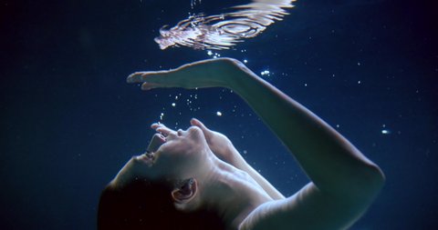 young woman is approaching to reflection of her face underwater