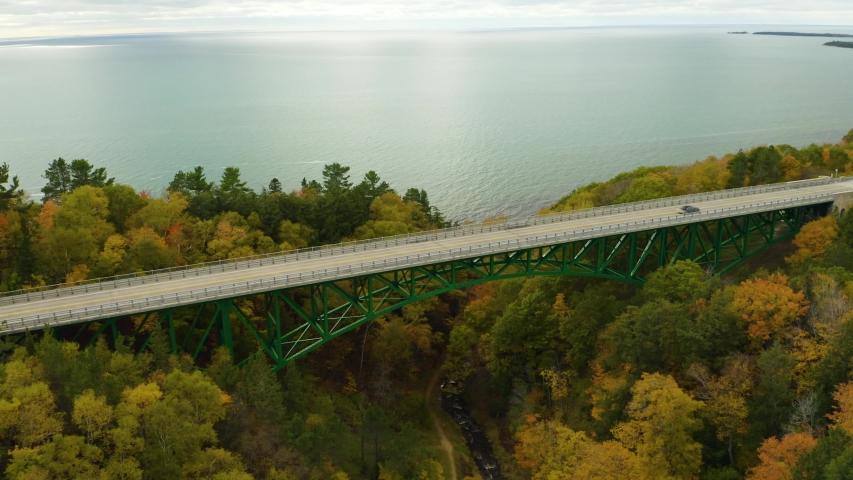 Aerial circling shot of green bridge along coast during peak fall foliage