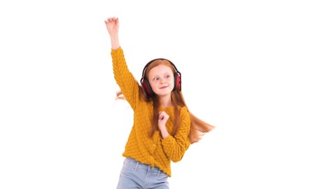 Little adorable foxy haired girl with charming smile listening to the music in wireless headphones and dancing. Child's positive emotions. Isolated, on white background