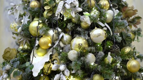 Classical decoration in golden and silver colours on new year pine, closeup view. Balls, toys and yellow garlands. Gimbal tilt up shot of artificial christmas green tree.
