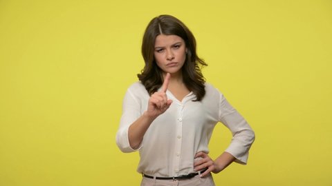 Be careful! Bossy strict businesswoman with brunette hair in blouse showing admonishing gesture, warning of danger, looking displeased asking be cautious. studio shot isolated on yellow background