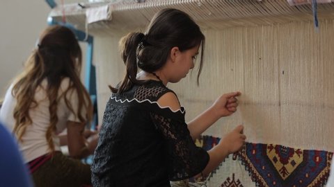 Azerbaijan, Baku - July 2019: Young oriental women sew carpet on a weaving machine with a hook. Handmade beautiful oriental rug. Girls work very quickly and efficiently