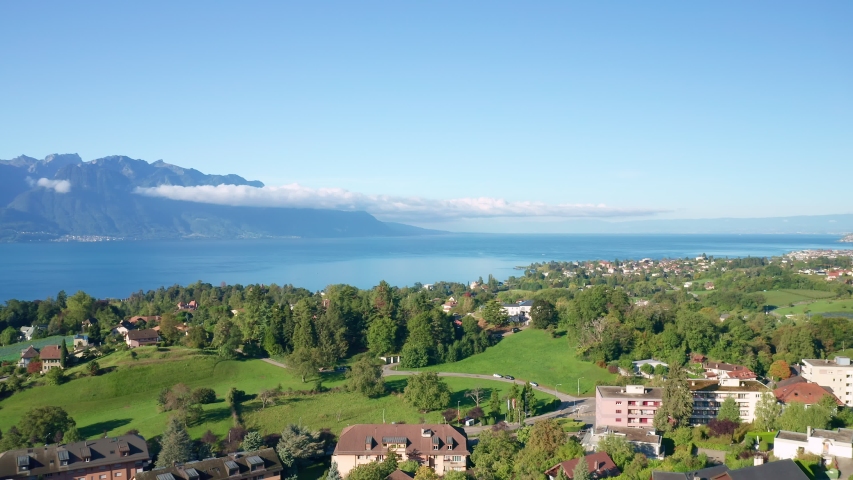 Drone flight at Montreux on the Lake Geneva shoreline. Aerial view of Switzerland at sunny day with clouds lying on the top of the mountains