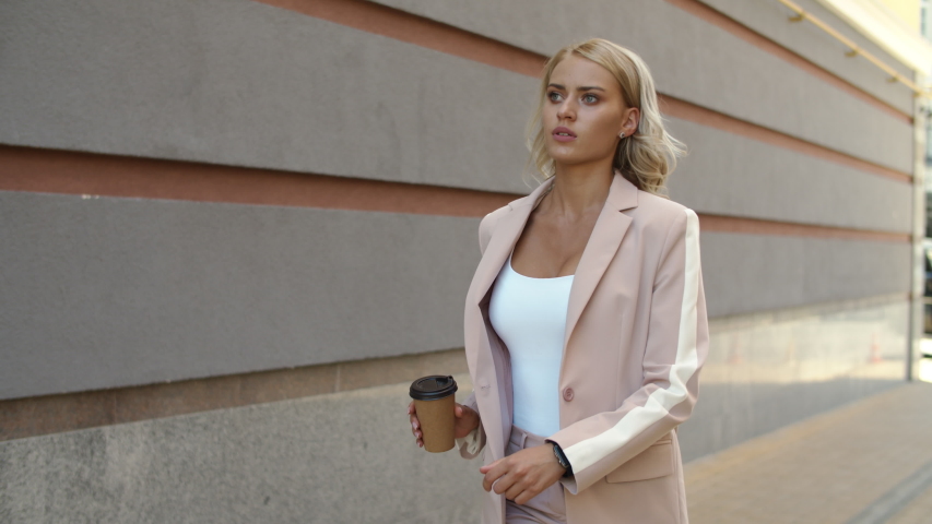 Close up serious woman walking in hurry at street. Pretty business woman watching time on smart watch outdoor. Stylish businesswoman walking with coffee at street. Office employee going to work