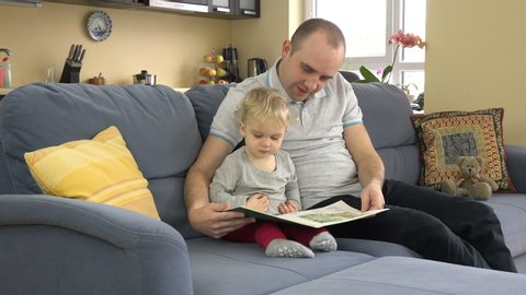 Lovely father reading story book with his baby at home. Toddler child boy education. Family man and son have fun together. Static closeup shot.