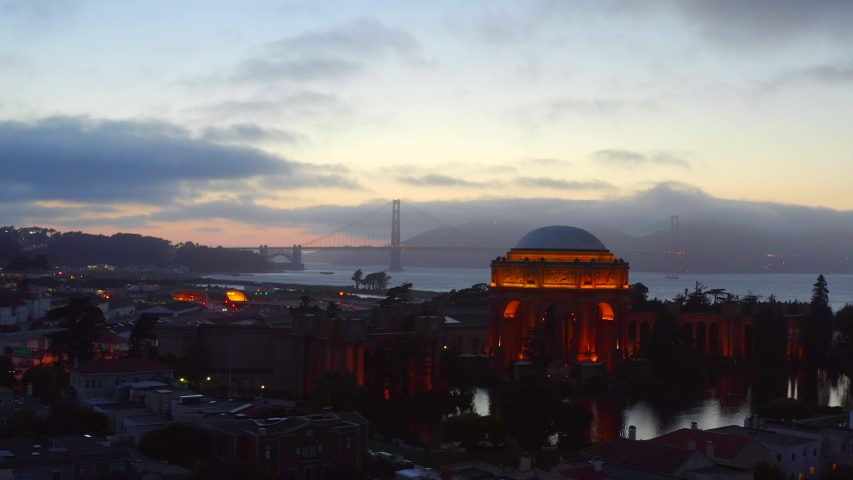 Aerial, rising, drone shot, panning over buildings, overlooking the crissy field beach, the presidio shoal and the Golden gate bridge, at dusk, summer evening, in San Francisco, California, USA