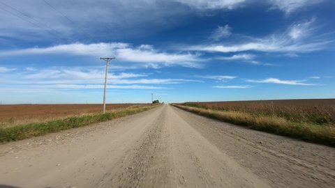 Point of view footage while driving down a gravel road in rural Iowa; visible are power lines, corn fields, barn, soybean fields and a wind turbines