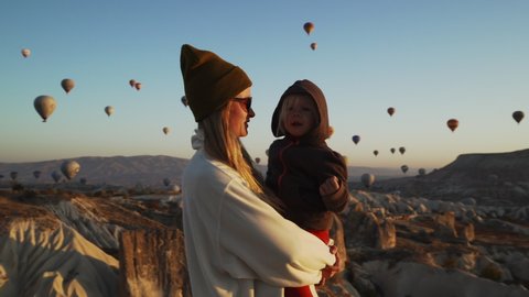 Young blond mother with her kid spinning around in front of air balloons