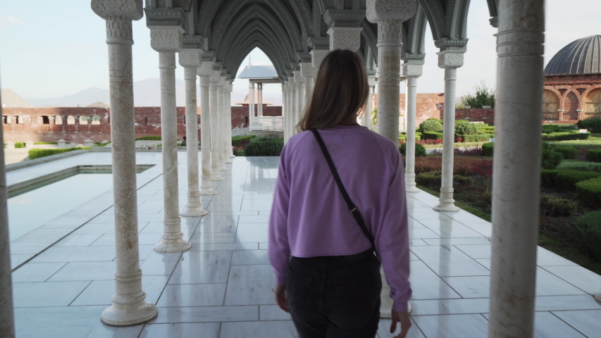 young blond caucasian female tourist walking through columned hall