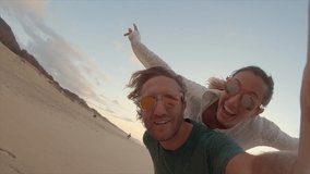 Couple taking cool selfies on the beach piggy back. Young people travelling taking selfies. Slow motion 