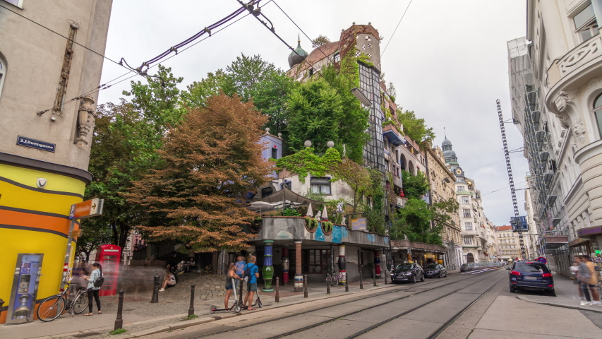 The Hundertwasserhaus apartment block timelapse hyperlapse has colorful facade, undulating floors, a roof covered with earth and grass, and large trees growing from inside the rooms. Vienna, Austria