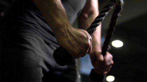 Close-up man pulls down rope on cable machine, pumping shoulders and lower chest