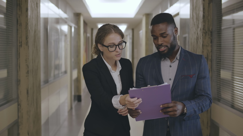 Multiracial young business people male and female discussing data from documents walking in office lobby before meeting. Royalty-Free Stock Footage #1043480839