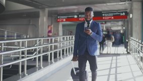 Elegant african businessman checking e-mail on mobile phone while walking with suitcase inside airport. Experienced male employer using cell phone while walking on train platform going for work travel - Powered by Shutterstock - Get 15% off with code: PIKWIZARD15